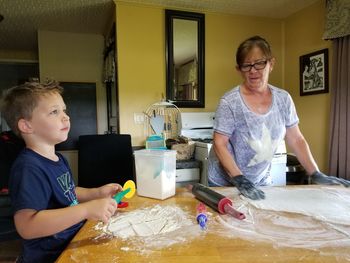 Senior woman with grandson preparing dough on table in kitchen at home