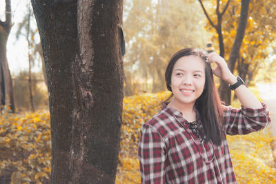 Portrait of smiling young woman standing by tree