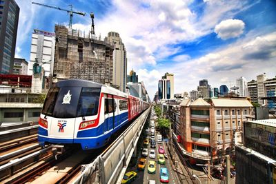 View of sky train by buildings and cars in city