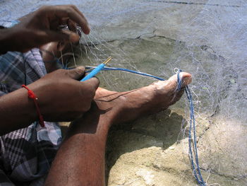 Low section of man knitting fishing net