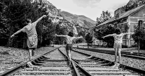 Rear view of father with daughters walking on railroad tracks against mountains