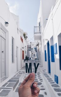 Cropped hand of person holding my text amidst buildings