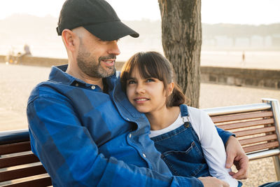 Father with arm around daughter sitting on bench