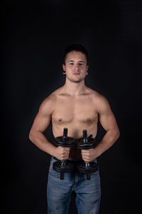 Portrait of shirtless man standing against black background