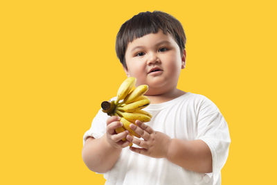 Portrait of boy holding ice cream against yellow background
