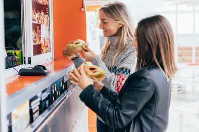 Two attractive girlfriends choosing and buying fast food ion a food truck in the street.