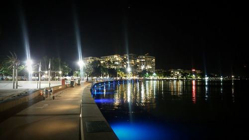 Illuminated city by river against clear sky at night