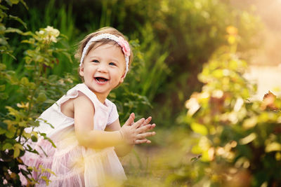 Side view of happy cute girl looking away while crouching against plants on field