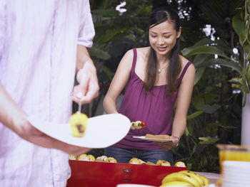 Young couple preparing food on barbecue grill against swimming pool