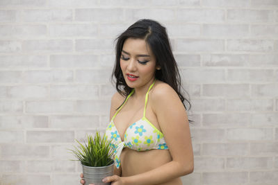 Sensuous beautiful woman holding potted plant while standing against wall