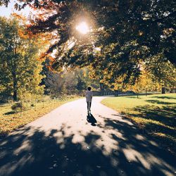 Rear view of woman walking on road at park on sunny day