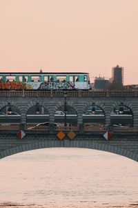Bridge over river by buildings against sky during sunset