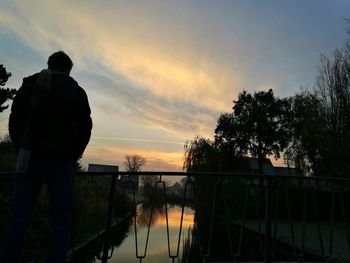 Rear view of silhouette man standing by railing against sky