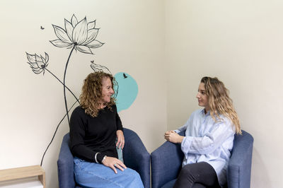Female coworkers smiling while relaxing sitting on armchairs during a break at work.