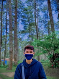 Portrait of young man standing against trees in forest