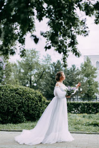 Beautiful bride in a wedding dress walks in a blooming apple-tree park in spring