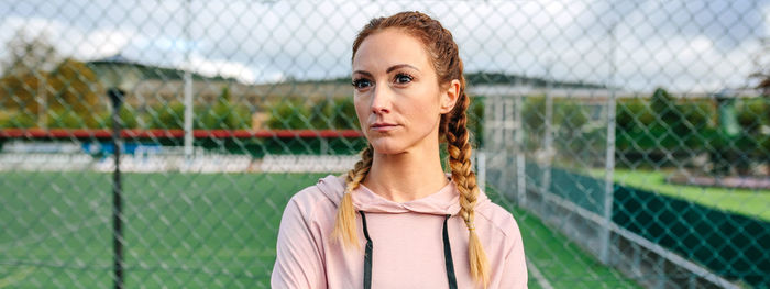 Portrait of young woman standing against chainlink fence