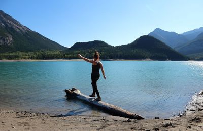 Woman walking on log in lake against clear sky