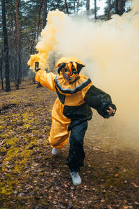 Full length of man wearing mask holding distress flare standing in forest