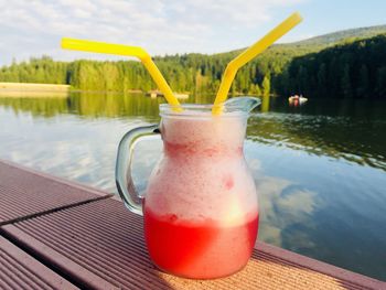 Orange smoothie in a jar with two straws placed on wooden pontoon near the lake