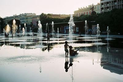 People on lake against buildings in city