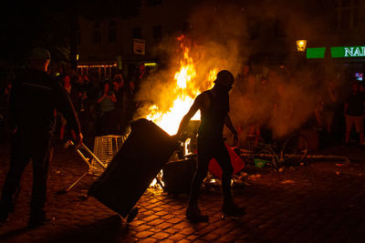 People standing by fire on street in city at night