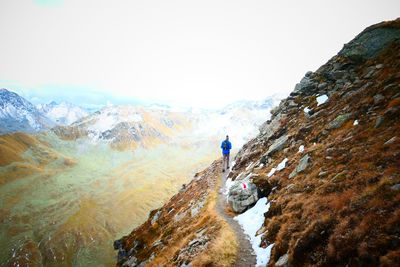 Man walking on rocky mountain against sky