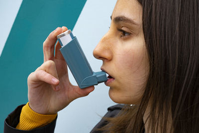 Woman inhaling a blue asthma inhaler on a blue background.