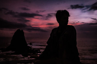 Silhouette man sitting by sea against sky during sunset