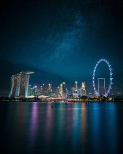 Illuminated city by river against sky