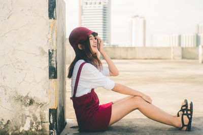 Side view of woman sitting against built structure