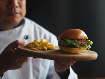 Midsection of chef holding burger and french fries