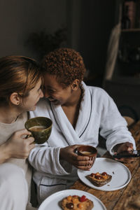 Happy non-binary couple enjoying while having breakfast at home