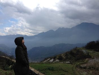 Woman standing by retaining wall against mountain range