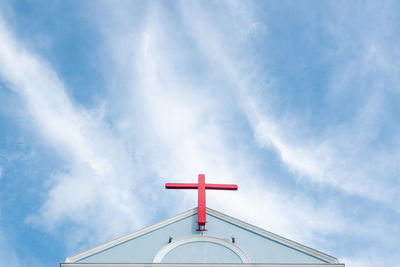 Church roof with red cross and blue sky.