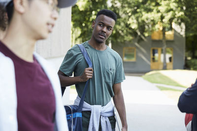 Thoughtful man carrying shoulder bag while walking with friends at university campus