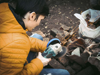 A young caucasian man in a yellow jacket is holding a drill and polishing with a disc