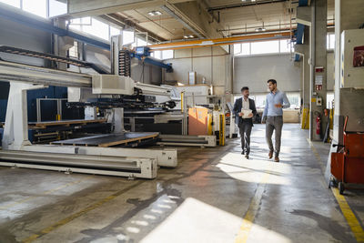 Businessman holding digital tablet while walking with colleague at factory