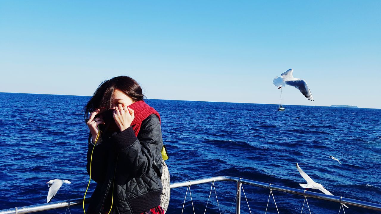 sea, clear sky, water, blue, leisure activity, lifestyles, young adult, horizon over water, copy space, standing, young women, vacations, person, casual clothing, full length, three quarter length, looking at camera, beauty in nature