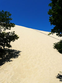 Low angle view of sand dunes against clear blue sky