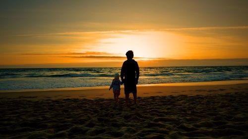 Silhouette man with son standing on sandy beach during sunset