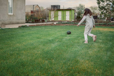 Cute little girl playing football with soccer ball on green lawn in backyard of house. child kicking