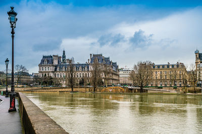 View of buildings by river against sky in city