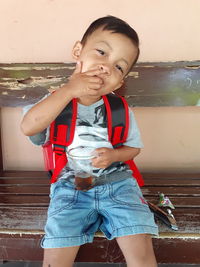 Portrait of cute boy siting on bench against wall