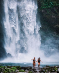 Friends wearing bikini walking against waterfall