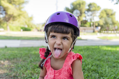 Little girl looking at camera while wearing protective helmet outdoors in a park.