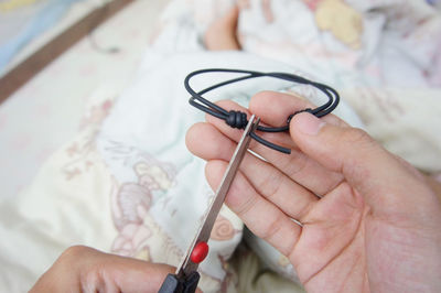 Cropped hands cutting cable on bed