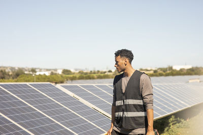 Young male engineer wearing reflective jacket while looking at solar panels at power station
