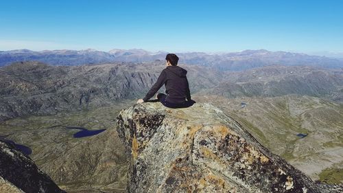 Rear view of man standing on rock against clear sky