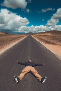 Man lying on road against sky